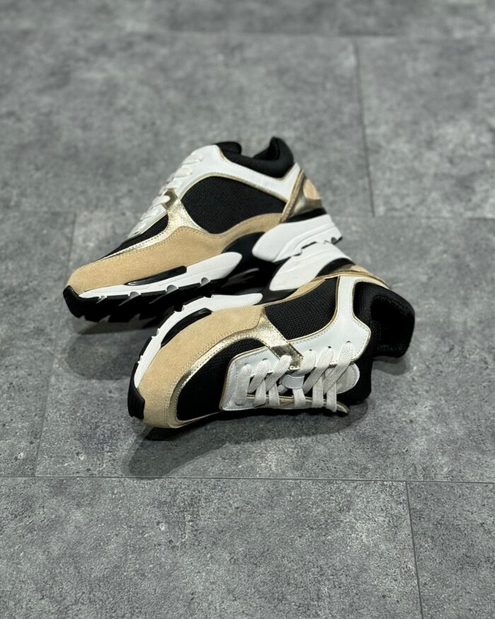 Sneakers streetwear beige e nero, design chunky e dettagli moderni su superficie grigia.
