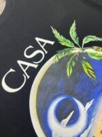 Maglietta tropicale con palmo, motivo circolare blu e giallo, e scritto CASA in bianco.