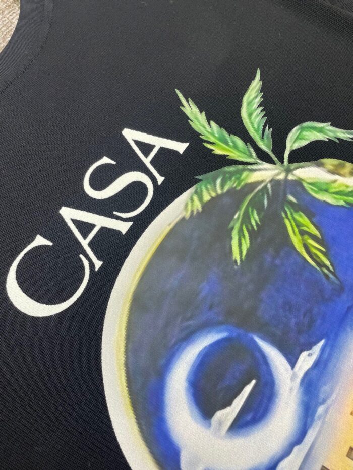 Maglietta tropicale con palmo, motivo circolare blu e giallo, e scritto CASA in bianco.