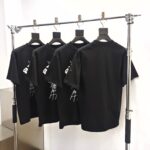 Magliette nere con logo, esposizione moderna su rastrelliera in metallo lucido.