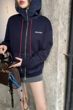 Donna in hoodie navy, gonna grigia, elegante borsa di lusso, sfondo urbano.