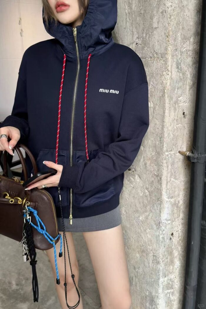 Donna in hoodie navy, gonna grigia, elegante borsa di lusso, sfondo urbano.
