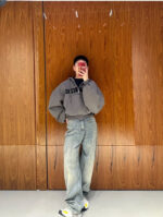 Persona in stile streetwear con hoodie oversized, jeans e sneakers, scatta selfie in ambiente moderno.