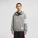 Giovane uomo con giacca sportiva grigia, stile moderno e casual, dettagli trendy e minimalisti.