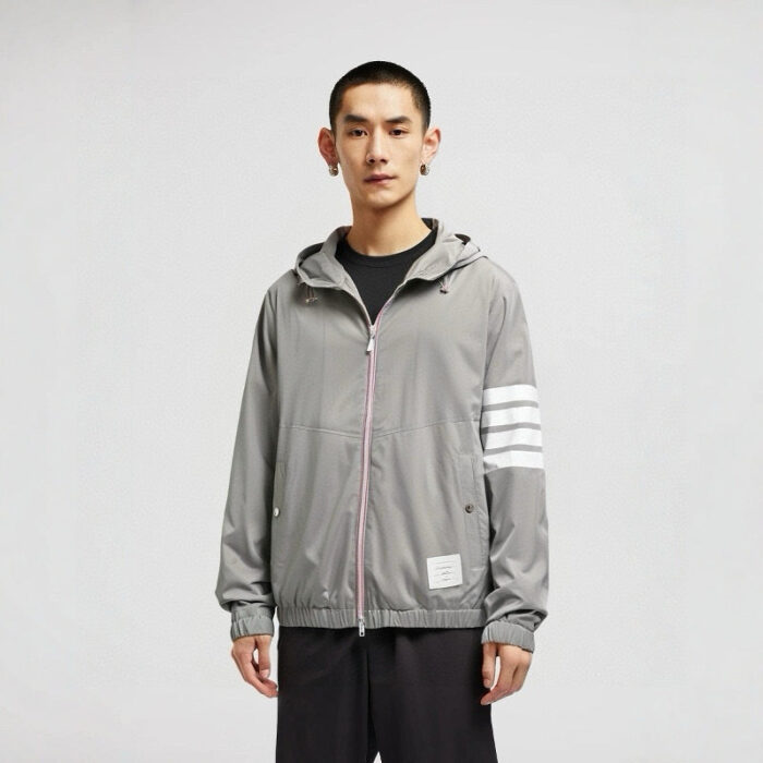 Giovane uomo con giacca sportiva grigia, stile moderno e casual, dettagli trendy e minimalisti.