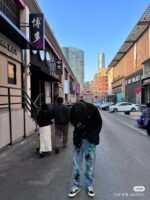 Street urbana multiculturale con negozi, persone, edifici moderni e tradizionali, giornata luminosa.