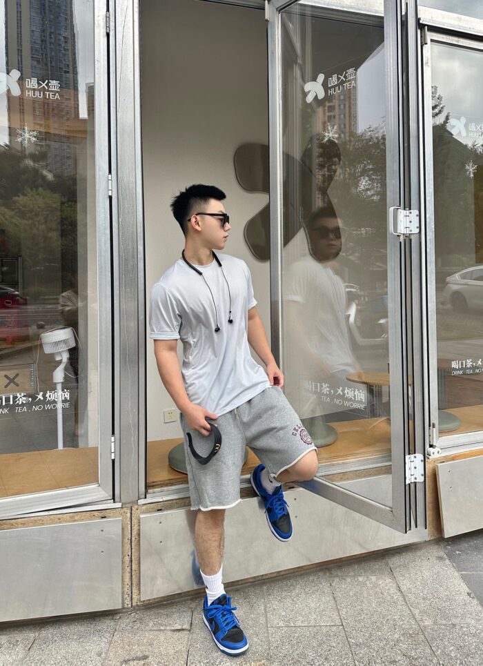 Giovane uomo sportivo davanti a negozio moderno in zona urbana con scarpe blu e occhiali.