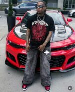 Uomo streetwear accanto a Chevrolet Camaro rossa, stile urbano, moda, auto sportiva e energia.