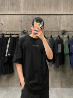 Selfie in stile streetwear con T-shirt oversize nera, cappellino e sfondo urbano.