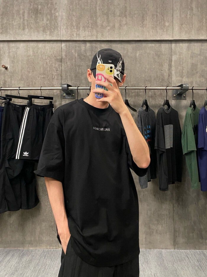 Selfie in stile streetwear con T-shirt oversize nera, cappellino e sfondo urbano.