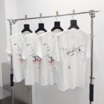 T-shirt bianche moderne con grafica urbana e design astratto, display minimalista su asta di ottone lucido.