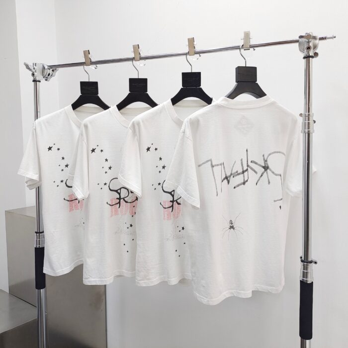 T-shirt bianche moderne con grafica urbana e design astratto, display minimalista su asta di ottone lucido.