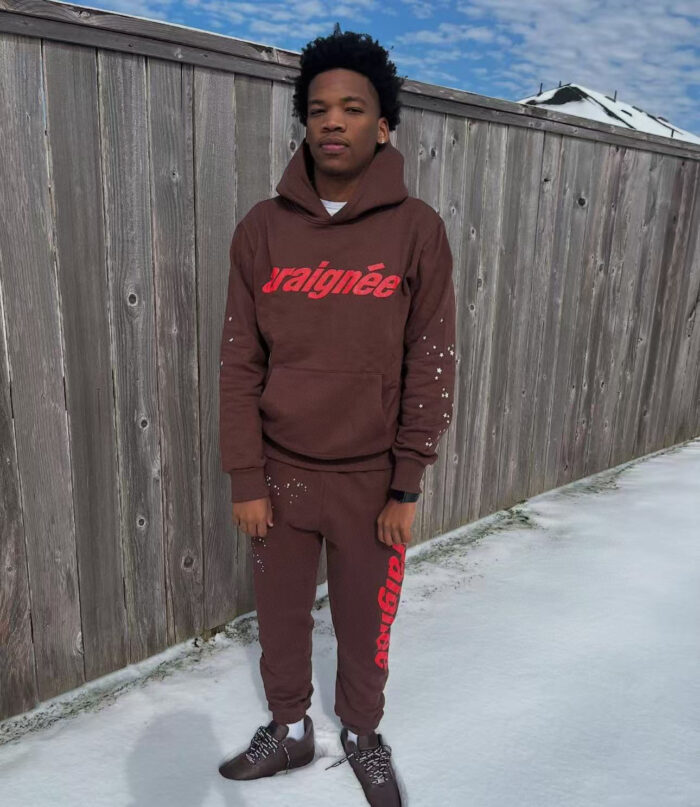 Giovane in streetwear invernale con hoodie, joggers e sneakers marroni sulla neve e cielo azzurro.