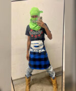 Selfie in stile urbano con outfit audace, gonna a quadri, foulard verde e stivali robusti.