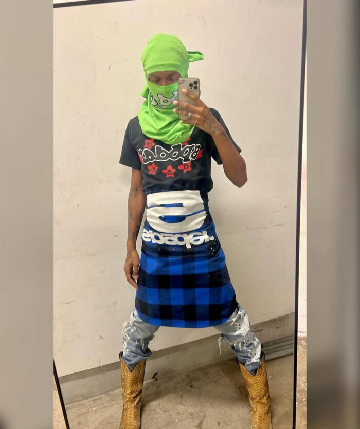 Selfie in stile urbano con outfit audace, gonna a quadri, foulard verde e stivali robusti.