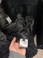 Giacca nera moderna con design artistico, dettagli trapuntati e etichetta di cura interna.