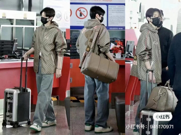 Viaggiatore elegante in aeroporto con giacca oversize, trolley silver e borsa di classe.