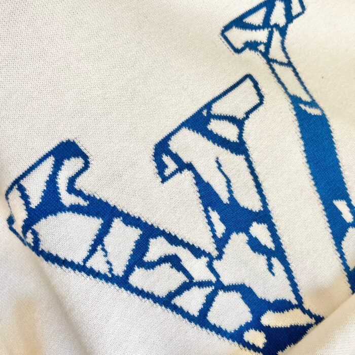 T-shirt con grande lettera V blu e dettagli artistici su tessuto bianco.