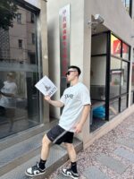 Giovane uomo con documenti davanti a edificio moderno, stile giovane e urbano.