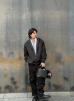Giovane uomo urbano con felpa nera e zaino, sfondo metallico rustico e moderno.