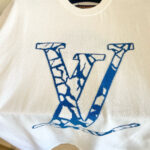 T-shirt bianca con grande V blu crackle e design ondulato, stile streetwear moderno.