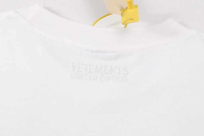 Maglietta bianca VETEMENTS con logo embossato e tag security gialla.