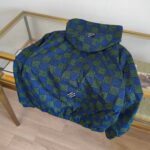 Giacca a quadri verde e blu con cappuccio, stile streetwear, su tavolo di vetro.