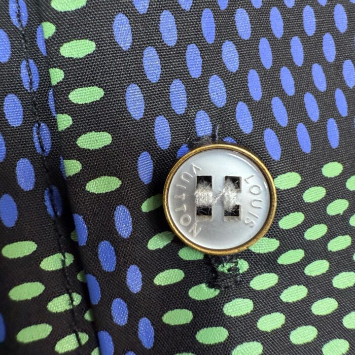 Tessuto nero con pois verdi e blu, bottone metallico moderno, dettagli eleganti e stile contemporaneo.