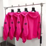 Giacche hoodie rosa fluo con grafica nera in esposizione moderna e minimalista.