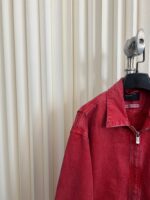 Giacca di jeans rossa su supporto nero, stile moderno e dettaglio elegante.