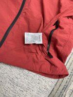 Giacchetto rosso sportivo con zip e etichetta di cura, ideale per outdoor e stile dinamico.