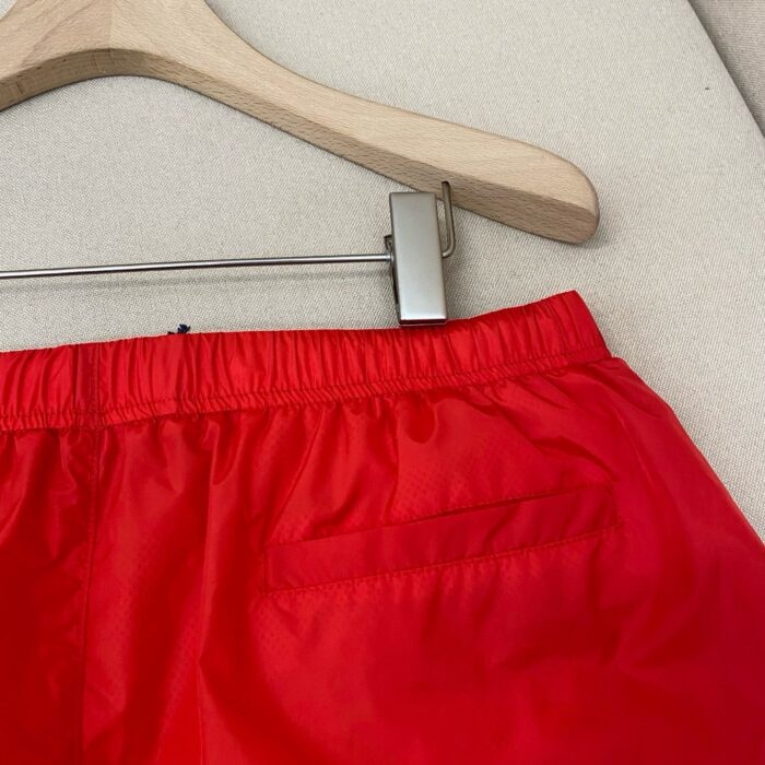 Pantaloncini sportivi rossi lucidi con elastic waistband e tasca, ideali per sport e relax.