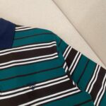 Polo teal a righe colorate, colletto blu navy e logo sottile, stile casual e raffinato.