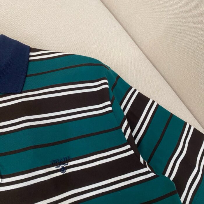 Polo teal a righe colorate, colletto blu navy e logo sottile, stile casual e raffinato.