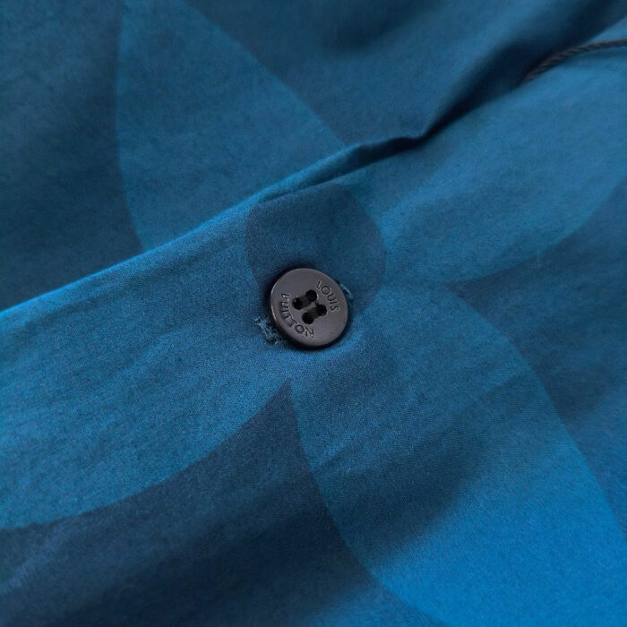 Dettaglio di camicia azzurra con bottone in plastica e motivo floreale elegante.