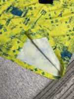 Tessuto giallo con disegni blu architettonici e decorativi, piegato su superficie neutra.