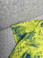 Camicia gialla con motivi artistici blu su sfondo tessile grigio, stile sofisticato e creativo.