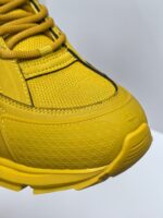 Scarpa sportiva gialla dettagliata, tessuto sintetico, suola ergonomica e lacci robusti.
