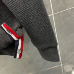 Maglione grigio con dettaglio a strisce colorate, bottoni e stile casual e sportivo.