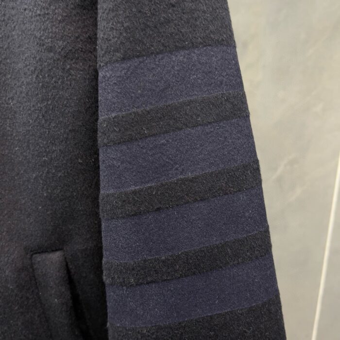 Manica di cappotto nero con strisce sovrapposte e tasca elegante, stile moderno e pratico.