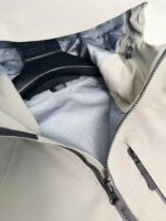 Giacca beige impermeabile con fodera grigia, zip resistente e tasche funzionali, stile e praticità.