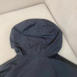 Giacca nera impermeabile con cappuccio minimalista e moderno, ideale per look pratici e stilosi.
