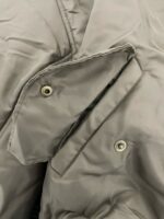 Giacchetto grigio impermeabile con tasche e bottoni metallici, dettaglio sartoriale e elegante.