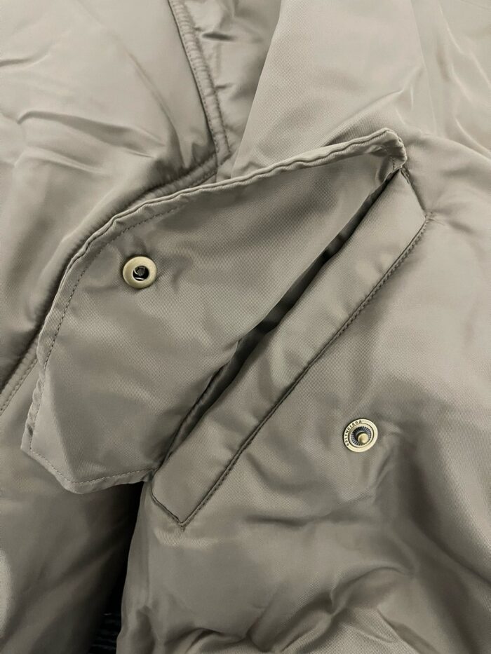 Giacchetto grigio impermeabile con tasche e bottoni metallici, dettaglio sartoriale e elegante.