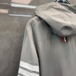 Giacca grigia sportiva con cappuccio, strisce bianche e dettaglio colorato sul collo.