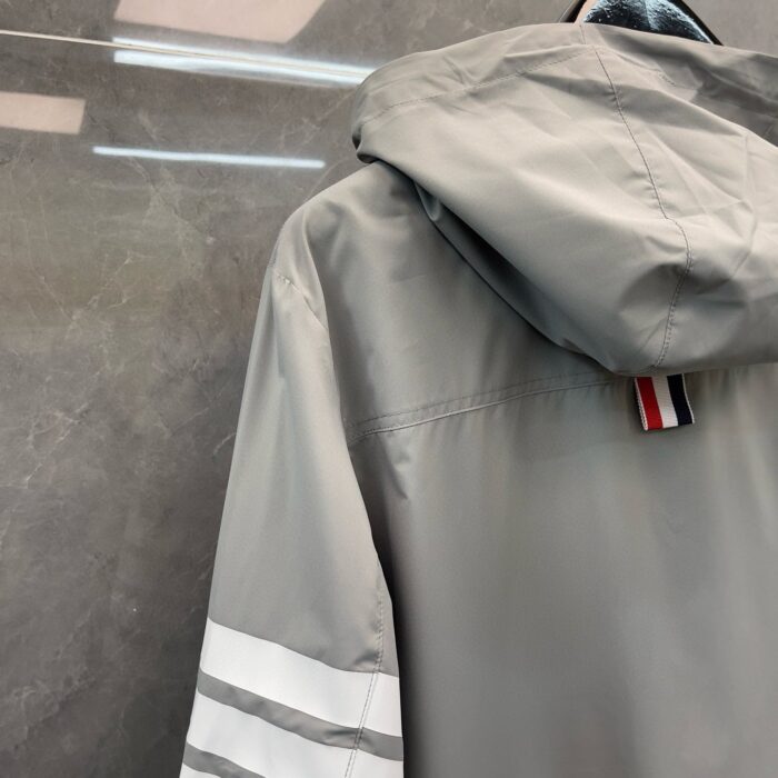 Giacca grigia sportiva con cappuccio, strisce bianche e dettaglio colorato sul collo.
