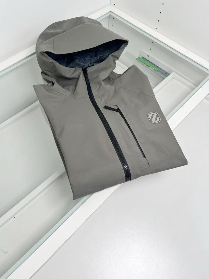 Giacchetto uomo grigio impermeabile, leggero, con cappuccio e tasca frontale, stile moderno.