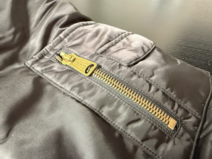 Giacca nera impermeabile con zip dorata e tasca nascosta, stile elegante e pratico.