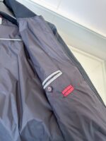 Interno di giacca sportiva impermeabile con strisce riflettenti e dettagli rossi innovativi.