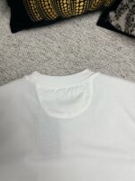 Maglietta bianca semplice su sfondo tessuto, ambiente accogliente e di stile casual elegante.